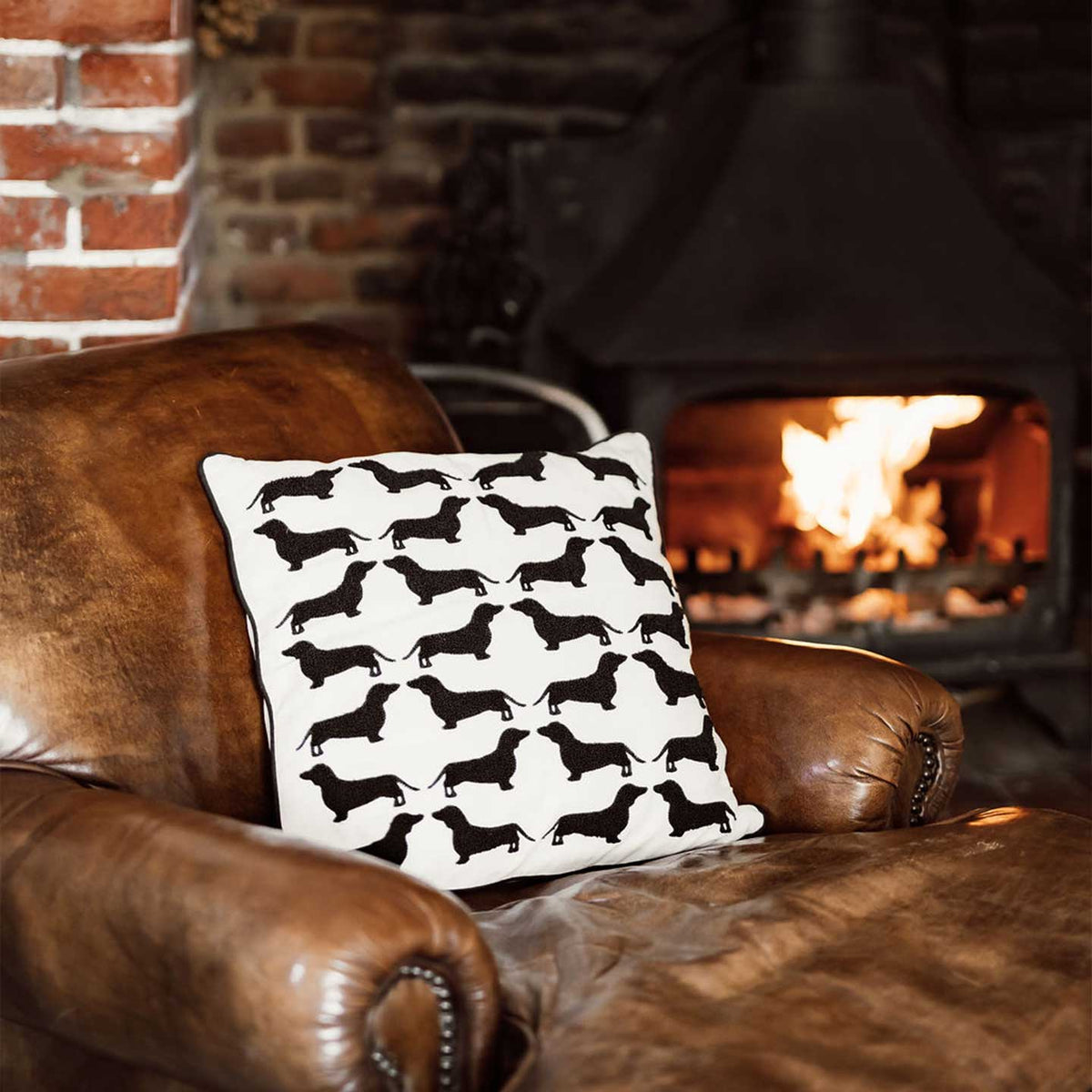 Black and cream Dachshund cushion on a leather armchair by a woodburner