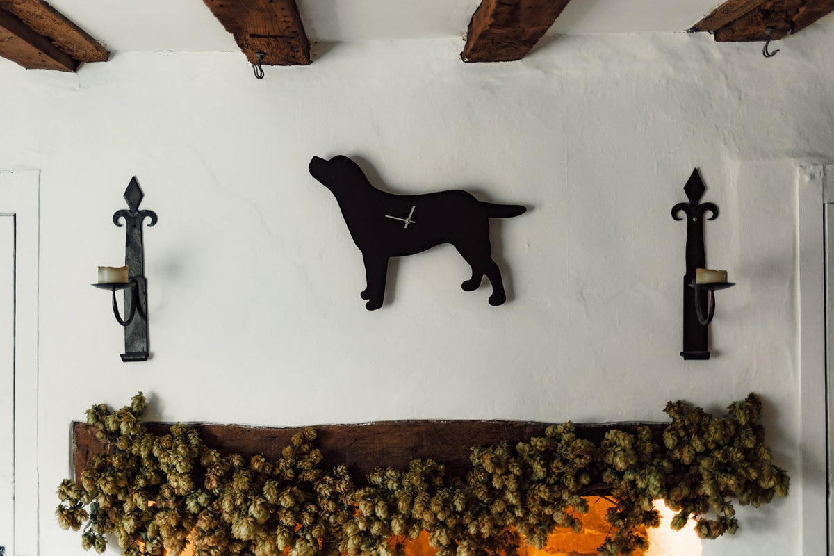 Black Labrador wagging tail clock on a whitewashed cottage wall between two iron sconces